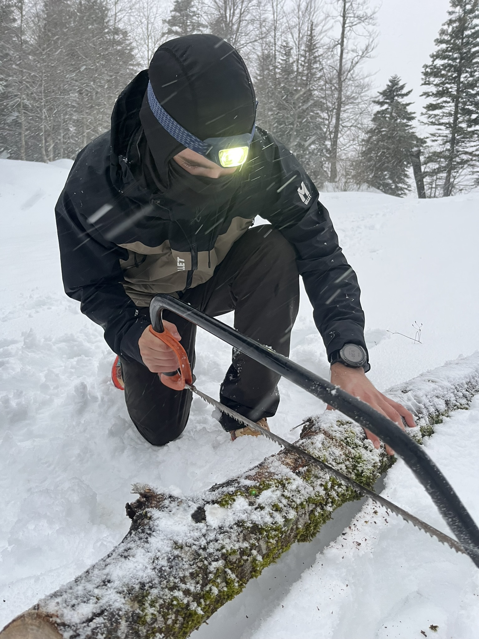Mathieu Ponton en train de scier du bois sous une tempête de neige pendant un bivouac hivernal en montagne